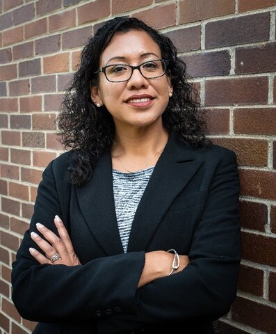 Portrait of Jacqueline Thomas standing in front of a brick wall with arms crossed.