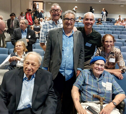 A group photo of people sitting and standing in an auditorium after a symposium.