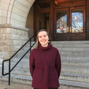 A photo of Susanna Barrett standing in front of the steps leading into the east entrance to Noyes Lab.