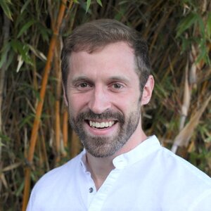 Head shot of new professor Ben Snyder with foliage in background.