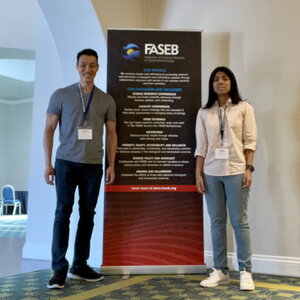 Jeff Chan and Melissa Lucero stand next to a vertical banner in an atrium of a building.