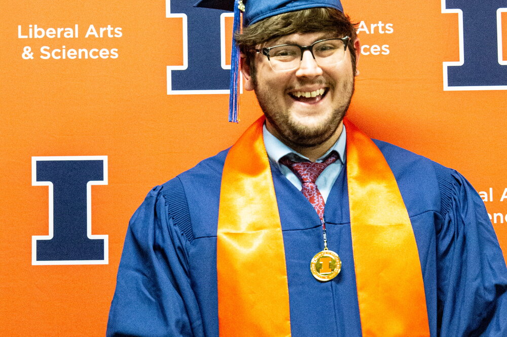 Ian Garvey in a cap and gown standing in front of an orange background