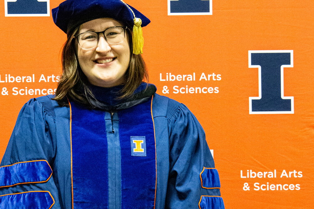 Amanda East in a cap and gown in front of an orange background